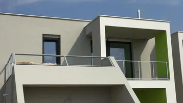 Modernes Gebäude mit Balkonen, Glasgeländer und hellen Fassaden unter blauem Himmel.