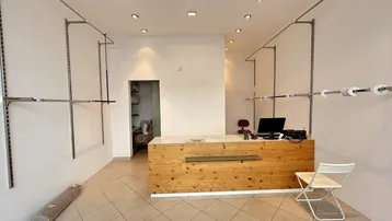 Heller Ladenraum mit Holztresen, weißen Wänden und flexiblen Kleiderstangen, ideal für ein Geschäft.