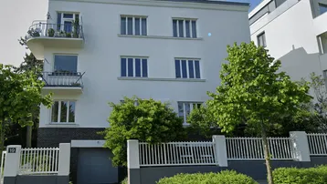 Weißes Mehrfamilienhaus mit Balkonen, Garage und gepflegtem Vorgarten in städtischer Umgebung.