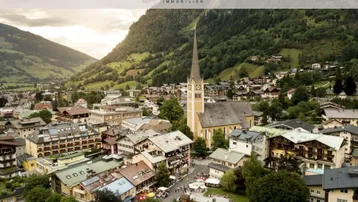 Panoramablick auf eine charmante Alpenstadt mit Kirche, umgeben von grünen Bergen.