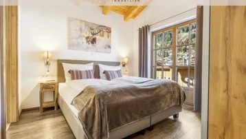 Gemütliches Schlafzimmer im alpinen Stil mit Holzbalkendecke und Bergblick durch das große Fenster.