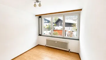 Helles Zimmer mit Laminatboden und Blick auf die umliegenden Häuser und Natur.
