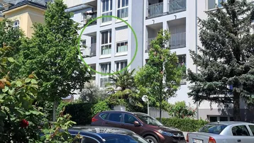 Modernes Wohngebäude mit Balkonen und großen Fenstern, umgeben von Grünflächen und parkenden Autos.