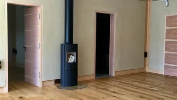 Heller Wohnraum mit Holzboden, beigen Wänden und einem modernen freistehenden Kaminofen.