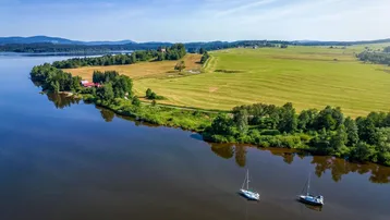 Idyllische Luftaufnahme einer weiten Seenlandschaft mit grünen Feldern und Wäldern unter blauem Himmel.