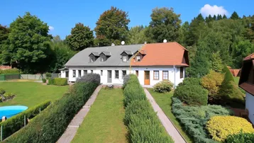 Großzügiges Anwesen mit gepflegtem Garten, Hecken und einem kleinen Pool unter blauem Himmel.