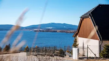 Haus mit Blick auf den See und die umliegenden Berge unter blauem Himmel.
