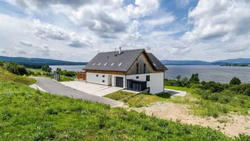 Neubau am Seeufer mit weitläufiger Grünfläche und Bergblick.