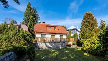 Haus mit rotem Ziegeldach, umgeben von hohen Nadelbäumen und einem gepflegten Rasen.