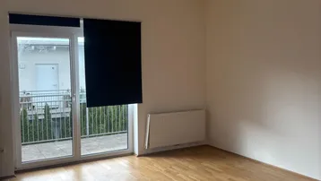 Helles Zimmer mit Holzboden und Zugang zu einem Balkon, ideal als Schlaf- oder Arbeitszimmer.