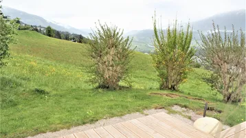 Weitläufiger Blick von der Holzterrasse über grüne Hügel und die umliegende Landschaft.