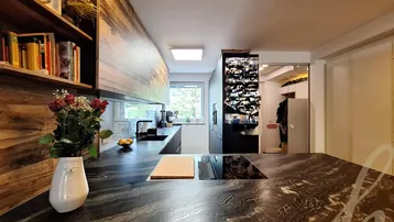 Moderne Küche mit dunkler Steinplatte, Holzelementen und integriertem Kochfeld, bietet einen Blick ins Grüne.