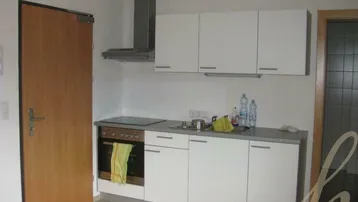 Kleine Einbauküche mit weißen Schränken, integriertem Backofen und Dunstabzugshaube.