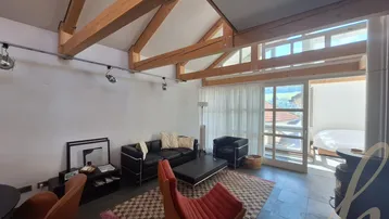 Helles Wohnzimmer mit Holzbalken, Kaminofen und Zugang zu einem verglasten Balkon.