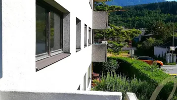 Blick vom Balkon auf die umliegende Berglandschaft und die benachbarten Gebäude.