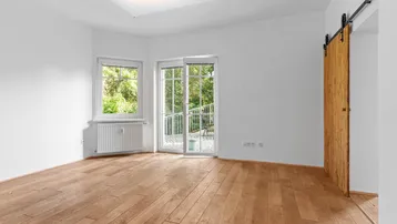 Heller Raum mit Holzboden, weißen Wänden und Zugang zu einem kleinen Balkon.