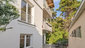Außenansicht des Gebäudes mit Balkonen, einer kleinen Terrasse und üppigem Grün.