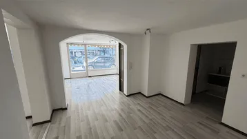 Heller, leerer Raum mit Holzboden und großem Bogen, der zu einem Schaufenster mit Straßenblick führt.