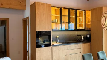 Moderne Holzküche mit schwarzen Arbeitsplatten, integriertem Backofen und offenem Übergang zum Essbereich.