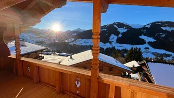 Sonniger Holzbalkon mit atemberaubendem Blick auf die verschneite Berglandschaft und umliegende Häuser.