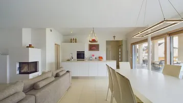 Heller, offener Wohn-Essbereich mit integrierter Küche, Kamin und Zugang zur Terrasse.