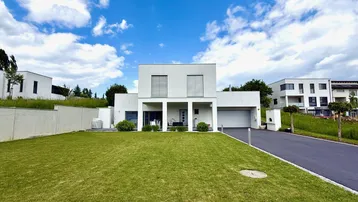 Moderne weiße Villa mit gepflegtem Rasen, Auffahrt und integrierter Garage unter blauem Himmel.