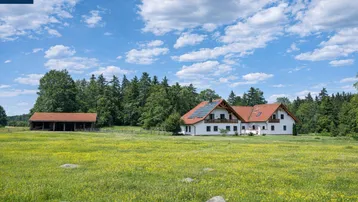 Großzügiges Anwesen mit weißem Haus, rotem Dach und weiten grünen Feldern unter blauem Himmel.