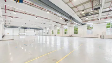 Große, leere Industriehalle mit Betonboden, hohen Decken und einem Laufkran, ideal für Lagerung oder Produktion.