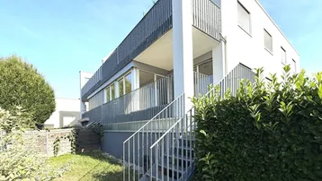 Modernes Mehrfamilienhaus mit weißer Fassade, Balkonen und Zugang zum Gartenbereich.
