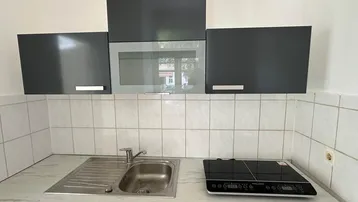 Moderne Küchenzeile mit Spüle, Induktionskochfeld und dunklen Hängeschränken über weißen Fliesen.