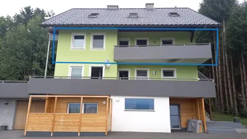 Mehrfamilienhaus mit hellgrüner Fassade, Balkonen und Dachgauben in ländlicher Umgebung.
