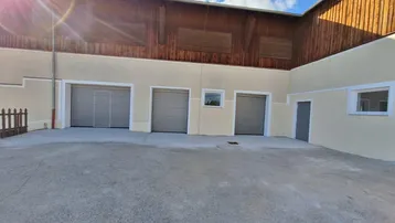 Außenansicht eines Gebäudes mit mehreren Garagentoren und einem großen gepflasterten Vorplatz unter blauem Himmel.