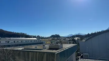 Panoramablick über die Stadt mit Bergen im Hintergrund unter strahlend blauem Himmel.