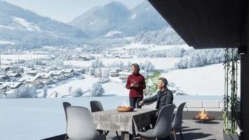 Gemütliche Terrasse mit Esstisch und Feuerstelle, bietet einen weiten Blick auf die verschneite Berglandschaft.