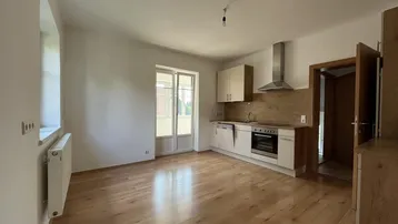 Helle offene Küche mit Holzboden, Einbaugeräten und Zugang zu einem Balkon oder einer Terrasse.