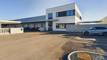 Moderne Gewerbeimmobilie mit weißer Fassade, großen Fenstern und ausreichend Parkplätzen im Freien.