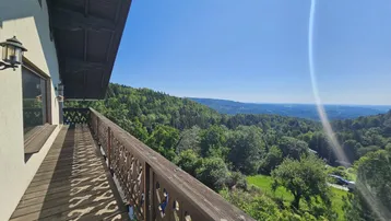 Langer Holzbalkon mit geschnitztem Geländer bietet einen weiten Blick über bewaldete Hügel und Täler.