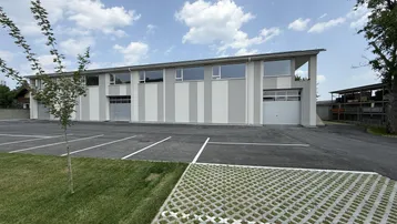 Modernes Geschäftsgebäude mit gestreifter Fassade und großem Parkplatz unter blauem Himmel.