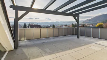 Große geflieste Terrasse mit moderner Überdachung und weitem Blick über die Landschaft und Berge.