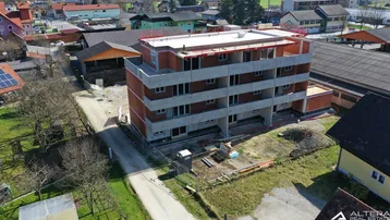 Luftaufnahme eines im Bau befindlichen Mehrfamilienhauses mit Rohbau und umliegender Bebauung.