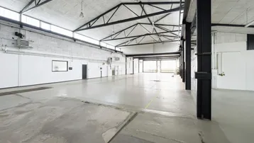 Geräumige Industriehalle mit hohen Decken, Betonboden und sichtbaren Stahlträgern, ideal für Lagerung oder Produktion.