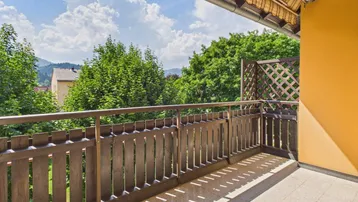 Geräumiger Balkon mit Holzbalkonbrüstung, Fliesenboden und schöner Aussicht auf die grüne Umgebung.