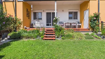 Große Terrasse mit Holzdeck und Gartenmöbeln, umgeben von einem gepflegten Rasen und Blumenbeeten.