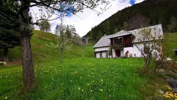Großzügiger Gartenbereich mit grüner Wiese und einem traditionellen Haus im Hintergrund, umgeben von Hügeln.