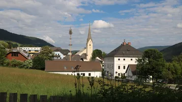 Panoramablick auf ein malerisches Dorf mit Kirche, umgeben von grünen Hügeln und Feldern.