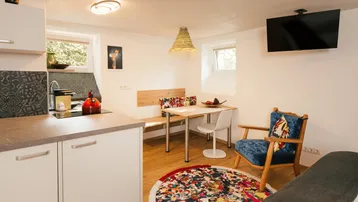 Helle, kompakte Wohnküche mit Essbereich, gemütlichem Sessel und Fernseher, ideal für kleine Apartments.