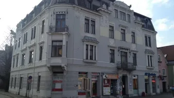 Historisches Eckgebäude mit klassischer Architektur und Geschäften im Erdgeschoss, an einer belebten Straße gelegen.