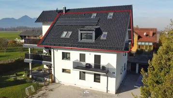 Modernes Mehrfamilienhaus mit Satteldach, Balkonen und Photovoltaikanlage in ländlicher Umgebung.