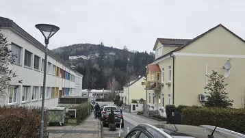 Blick auf die Straße und die umliegenden Gebäude mit bewaldetem Hügel im Hintergrund an einem bewölkten Tag.