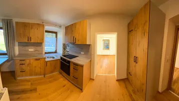Moderne Küche mit Holzfronten, integrierten Geräten und Blick in einen weiteren Raum.